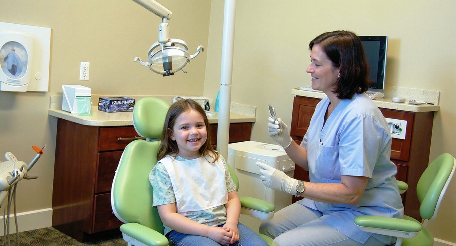 A pediatric dentist shows a young girl a dental mirror before her check-up at Lakes Pediatric Dentistry