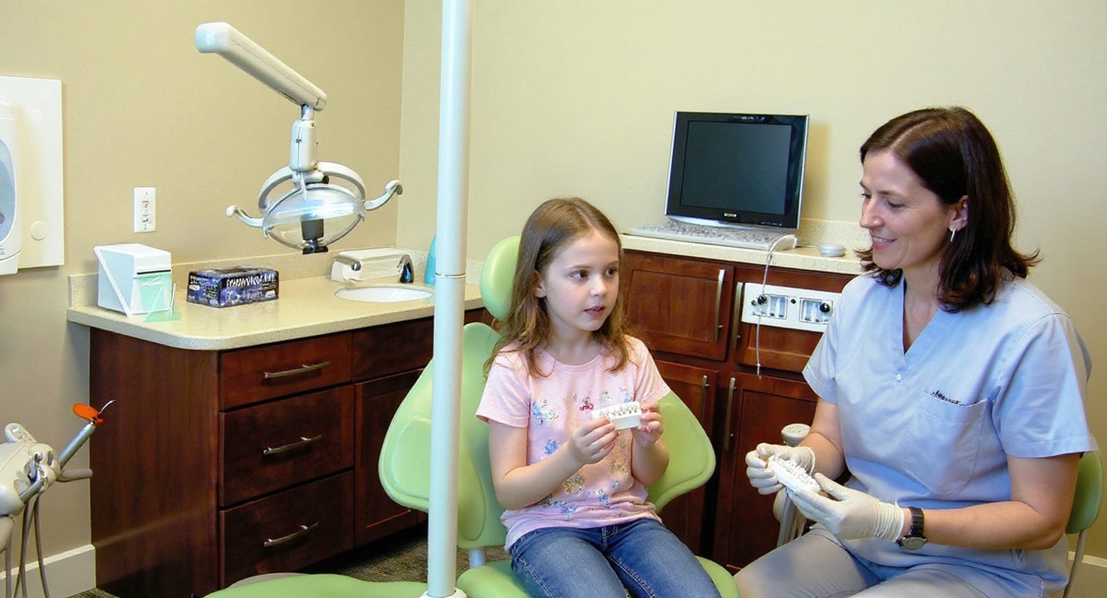 A pediatric dentist explains an extraction to a girl using a model of teeth at Lakes Pediatric Dentistry